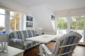 A room with a sofa, a dining table, and chairs, large windows with curtains, and framed pictures on the wall. - Holiday apartment with 2 bedrooms (Norden-Norddeich)