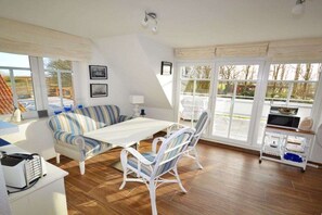 A room with a dining table, striped sofa, and chairs, large windows, and a white ceiling. - Holiday apartment with 2 bedrooms (Norden-Norddeich)