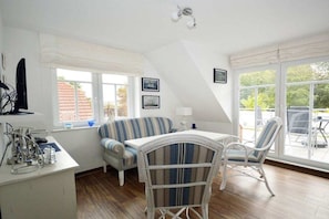 A room with a dining table, two chairs, a sofa, and a window with a view of the outside. - Holiday apartment with 2 bedrooms (Norden-Norddeich)