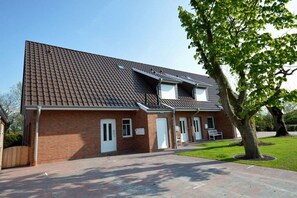 Een tweelaags gebouw van baksteen met een pannendak en een veranda, met een boom op de voorgrond.