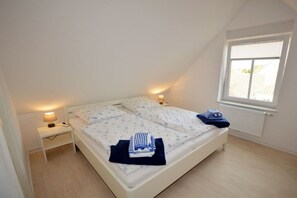 A single bed with a white headboard, a bedside table with a lamp, and a window with blinds. - Holiday apartment with 2 bedrooms (Norden-Norddeich)