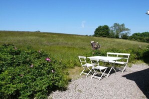 Un espace recouvert de gravier, avec une table et des chaises en métal blanc, entouré de verdure et sous un ciel dégagé.