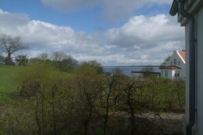 A view of a house with a red roof, a body of water in the background, and a grassy area with trees. - Holiday apartment with 3 bedrooms (Wohlenberg)