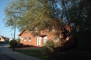 A two-story brick building with a central entrance, surrounded by trees and a sidewalk. - Holiday home with 1 bedroom (Boltenhagen)