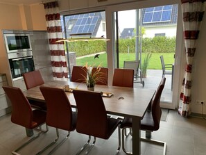 A modern kitchen with a dining area, large windows, and solar panels visible outside. - Villa Seegefluster (Goehren-Lebbin)