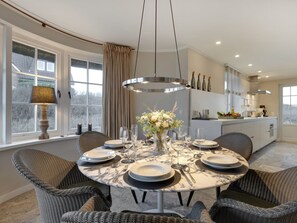 A dining area with a round table set for six, surrounded by wicker chairs, a chandelier, and a vase with flowers. - Bals Seedune 9a Sturmhues (Wenningstedt-Braderup)