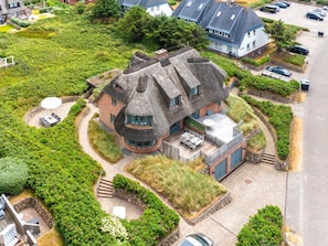 A house with a thatched roof, surrounded by lush greenery and a paved driveway. - Bals Seedune 9a Sturmhues (Wenningstedt-Braderup)