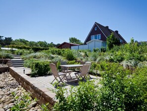 A house with a red roof and white walls, surrounded by a garden with a patio and outdoor furniture. - Nordhelmeck 6 Below (Norderney)