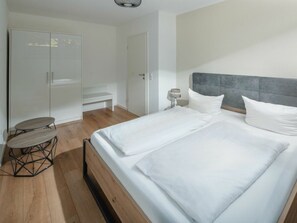 A bedroom with a bed, a bedside table, a lamp, a wardrobe, and a bench. - Nordhelmeck 6 Below (Norderney)