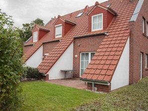 A two-story house with a sloped roof, brick exterior, and a small patio area. - Holiday Home With 3 Bedrooms (Krummhoern)