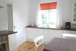 A kitchen with white cabinets, a wooden countertop, a window with a red blind, and a coffee maker. - Holiday apartment with 2 bedrooms (Wohlenberg)