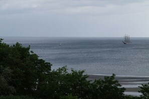 Eine Küstenlandschaft mit einem Schiff und einer Segelyacht auf dem Wasser, umgeben von Bäumen.