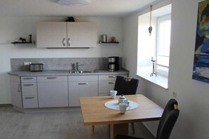 A compact kitchen with a dining area, a coffee machine, and a window with a view. - Holiday home with 1 bedroom (Nordstrand)