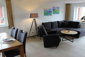 Ett modernt vardagsrum med en soffa, fåtöljer, ett matbord och konstverk på väggen.
