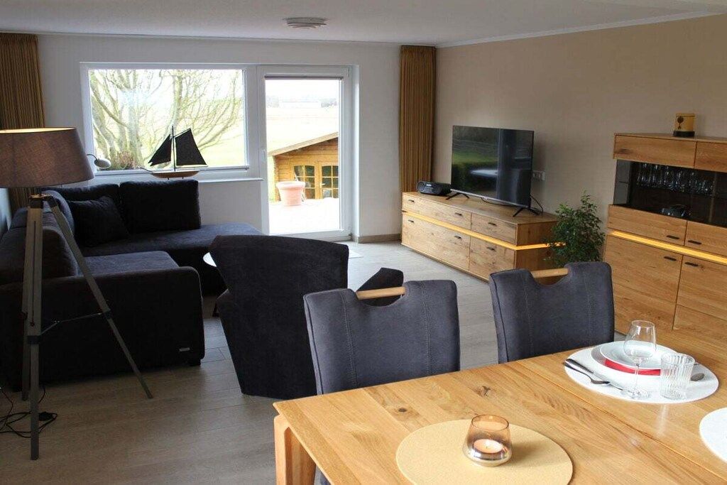 Una sala moderna con sofá, sillas, una mesa de comedor, televisor y una cocina con armarios y una planta.