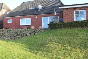 A brick house with a stone wall, a satellite dish, and a well-maintained lawn. - Holiday home with 1 bedroom (Nordstrand)