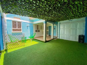 A covered outdoor area with artificial grass, a green chair, and a white garage door. - Beautiful spaces 3 bedroom bungalow (Kampala)