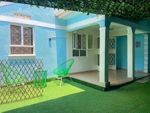 A blue house with a covered porch, artificial grass, and a green chair. - Beautiful spaces 3 bedroom bungalow (Kampala)