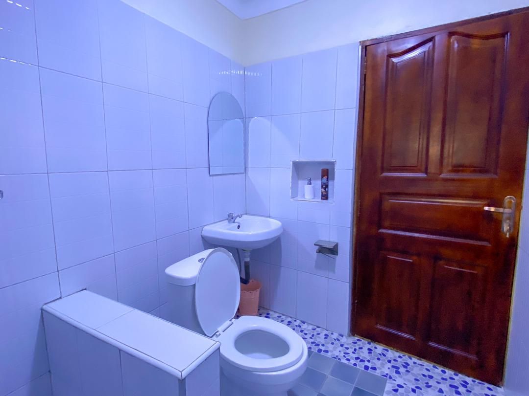 A bathroom with a toilet, sink, mirror, and wooden door.