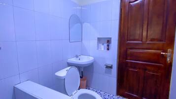 A bathroom with a toilet, sink, mirror, and wooden door.