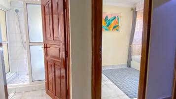 A room with a wooden door, a shower area, and a colorful abstract painting on the wall.