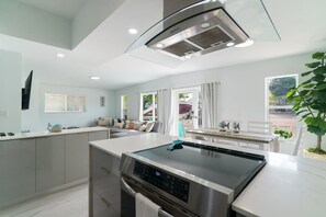 Una cocina moderna con horno integrado, un comedor con mesa y sillas, y vistas al exterior a través de las ventanas.