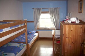 A room with bunk beds, a wooden desk, a radiator, and a window with curtains. - Margarethenhof - No. 2 (Tetenbüll)