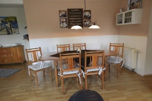 A dining area with a wooden table and chairs, a sign listing coffee options, and a radiator. - Margarethenhof - No. 2 (Tetenbüll)
