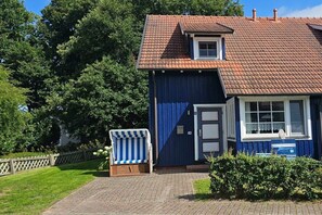 A two-story house with a red-tiled roof, a blue exterior, and a small porch with a striped chair. - Holiday home in Prerow with swimming pool (Prerow)