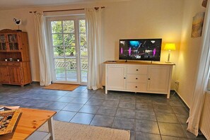 A living room with a television, a cabinet, a coffee table, and a view through a glass door. - Holiday home in Prerow with swimming pool (Prerow)