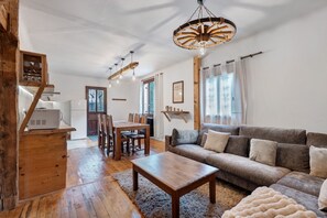 A spacious living area with a wooden dining table, a sofa, and a ceiling light fixture. - Apartment 'Appartement de montagne' (Queige)