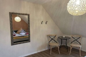 Ein Zimmer mit einem Bett, einem Spiegel, zwei Stühlen, einem kleinen Tisch und einer Hängelampe.
