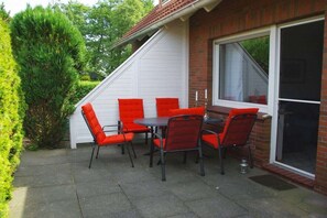 Eine Terrasse im Freien mit Tisch und Stühlen, einer Ziegelwand und einem großen Fenster.