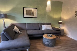 Ein Wohnzimmer mit Ecksofa, einem runden Couchtisch und einem gerahmten Bild an der Wand.