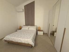 Ein Schlafzimmer mit einem Bett, Nachttischen, einem Kleiderschrank und einer Klimaanlage.