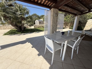 Eine Terrasse im Freien mit einem Glastisch und weißen Stühlen, umgeben von einer Steinmauer und Pflanzen.