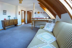 A cozy room with a sofa, a wooden cabinet, and a kitchen area with a window. - In the house Sommergarten 2 (Norderney)