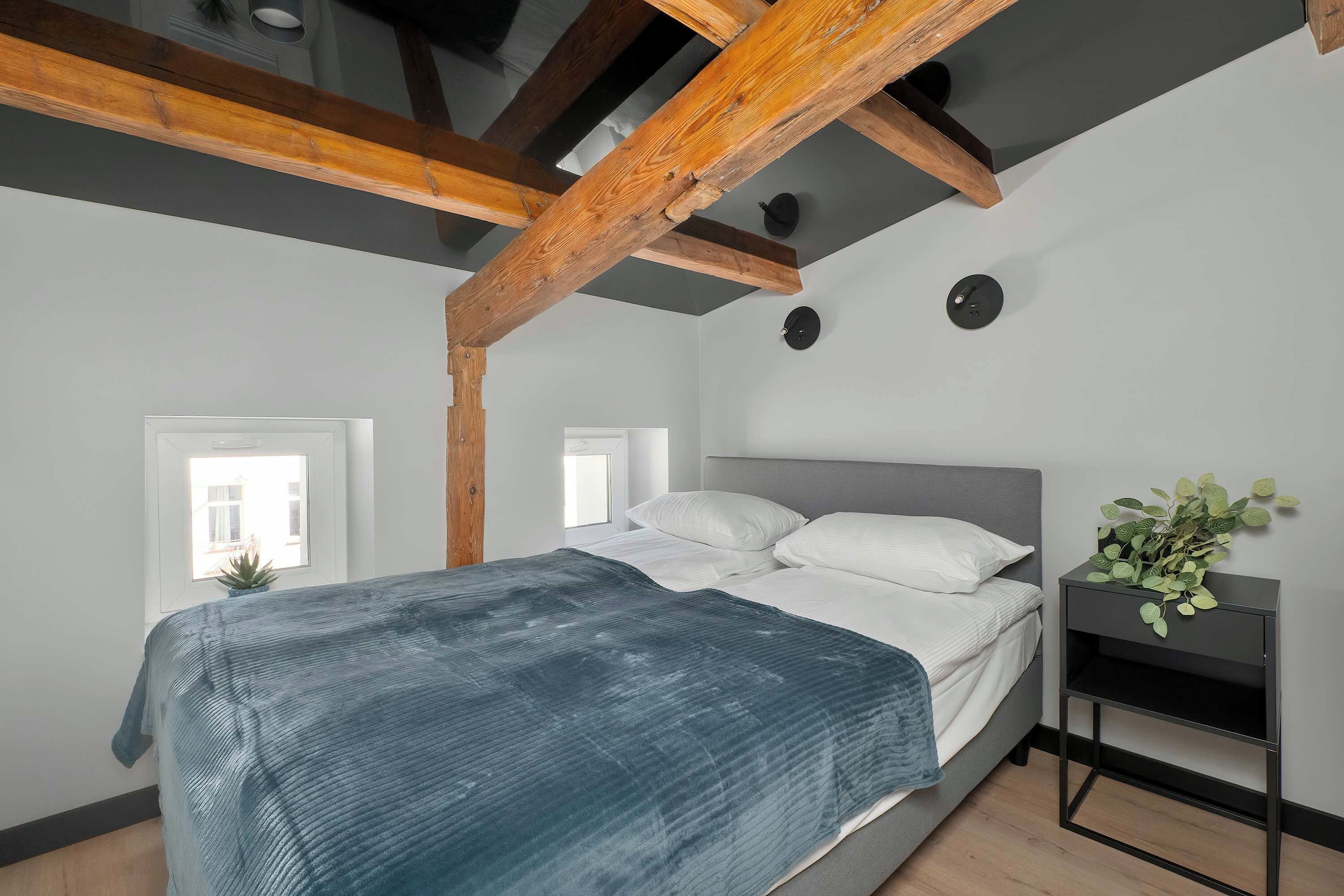Ein Schlafzimmer mit einem Bett, einem Nachttisch, einer Topfpflanze und freiliegenden Holzbalken.