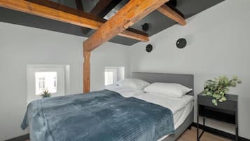 Ein Schlafzimmer mit einem Bett, einem Nachttisch, einer Topfpflanze und freiliegenden Holzbalken.