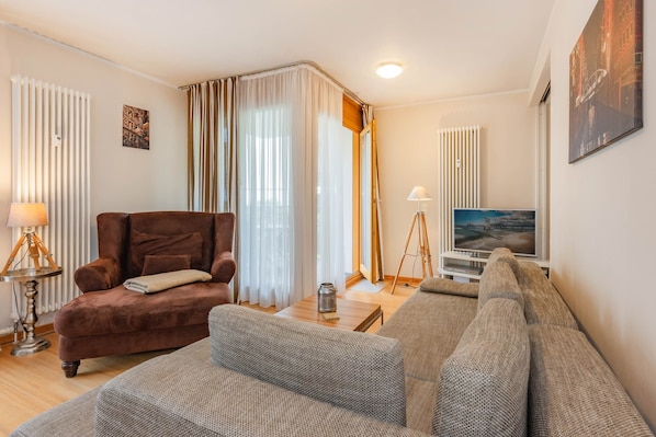 Ein Wohnzimmer mit einem braunen Sessel, einem grauen Sofa und einem Fernseher auf einem Schrank.