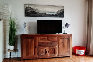 A wooden cabinet with a television and a lamp, a potted plant, and a painting on the wall. - Holiday home in Emden with swimming pool (Emden)