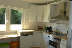 A compact kitchen with white cabinets, a stove, a sink, and a window providing natural light. - Holiday home in Emden with swimming pool (Emden)