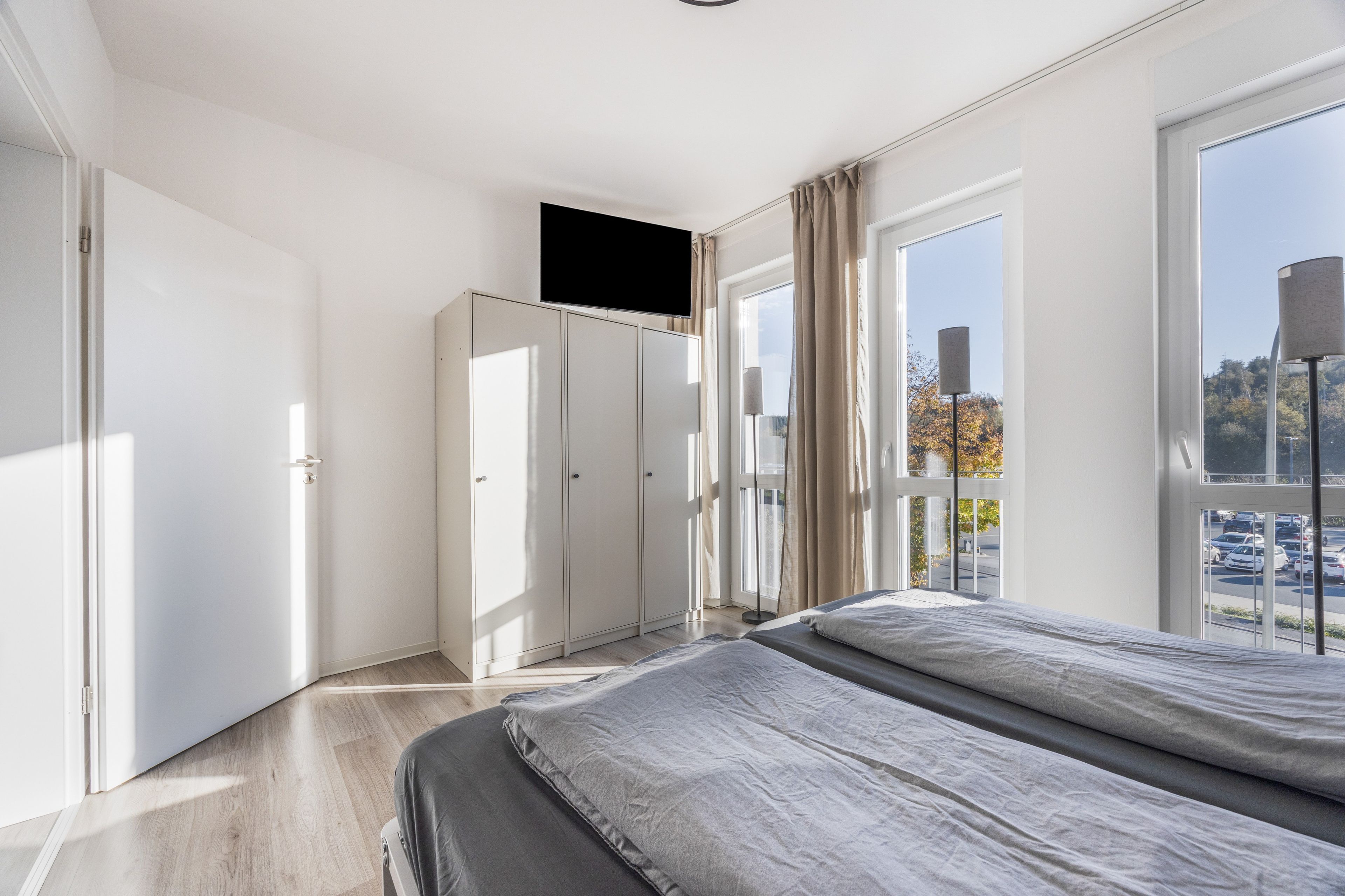 Ein modernes Schlafzimmer mit Bett, Kleiderschrank und einem an der Wand befestigten Fernseher.