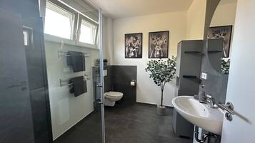 Une salle de bain moderne avec une douche à parois de verre, des toilettes, un lavabo et une plante en pot.