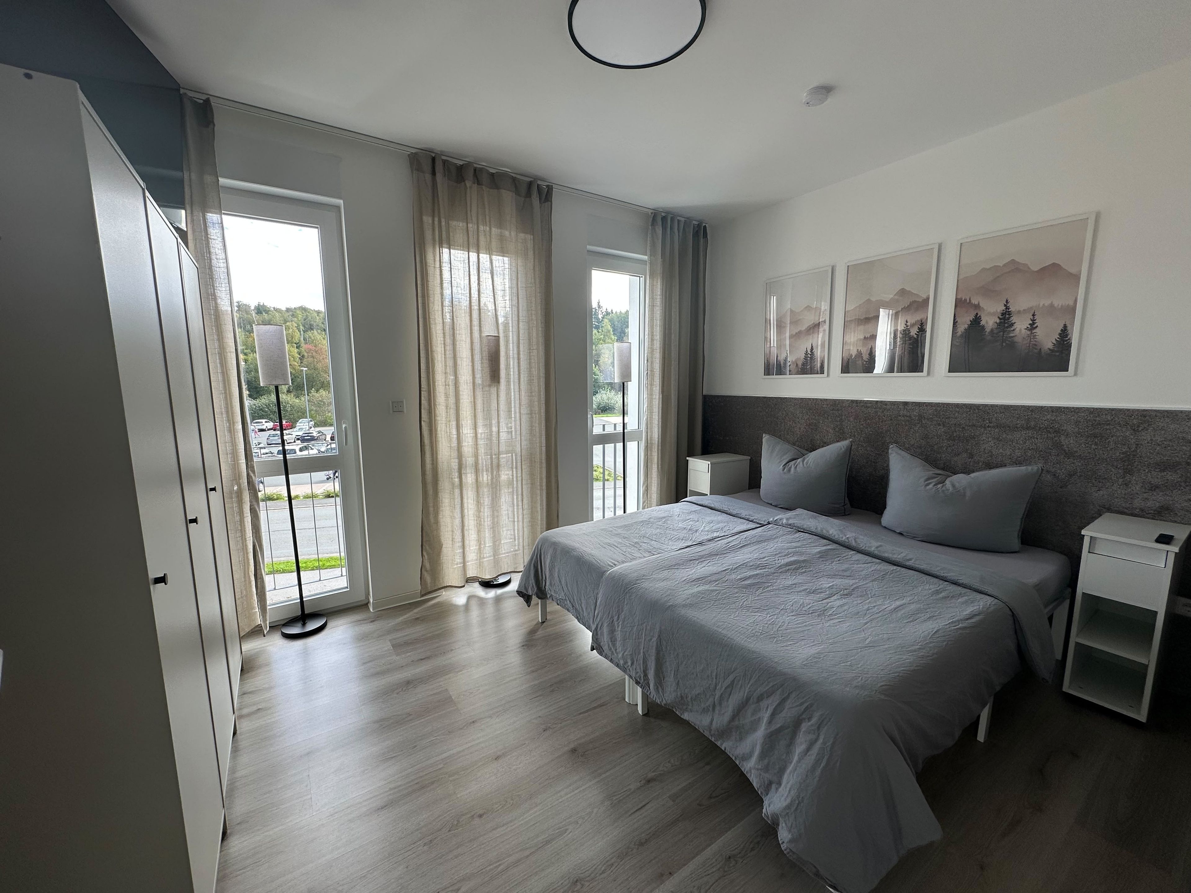 A modern bedroom with a large bed, bedside tables, and a view of the outdoors through a sliding door.