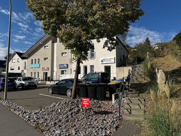 Een gebouw met verschillende borden, waaronder één voor een makelaarskantoor en een ander voor een meubelzaak. Voor het gebouw staan geparkeerde auto's en staat een boom.