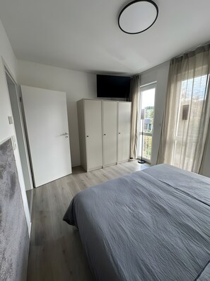 Ein Schlafzimmer mit Bett, Kleiderschrank und einem an der Wand befestigten Fernseher.