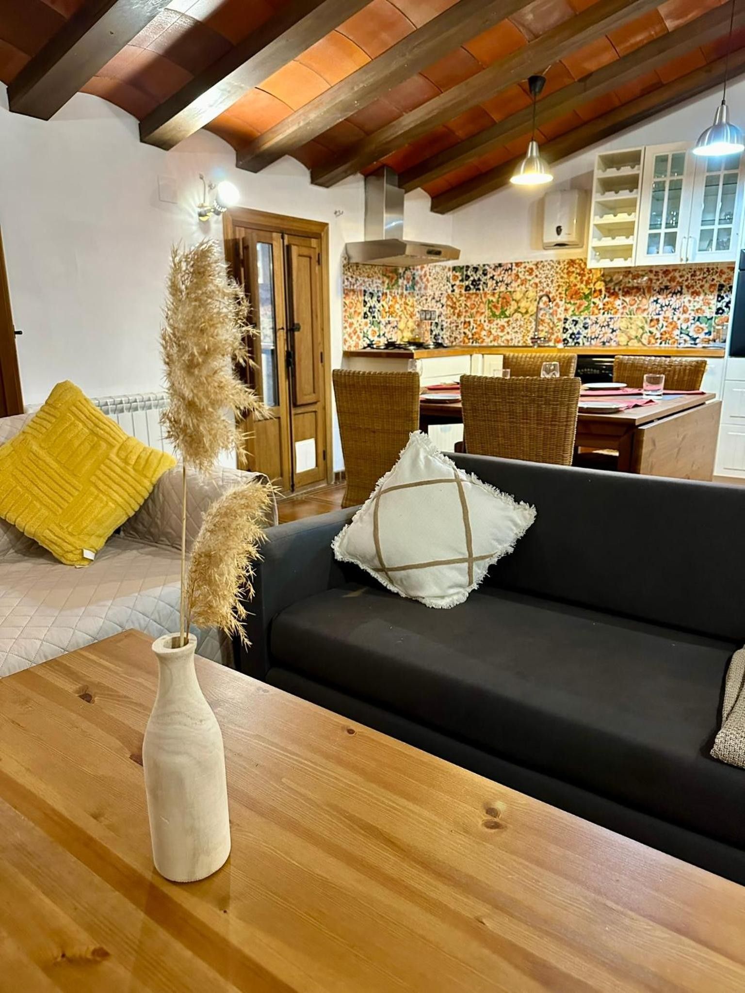 Een woonkamer met een donkere bank, een houten salontafel en een vaas met pluimgras.