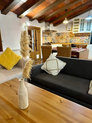 Una sala de estar con un sofá oscuro, una mesa de centro de madera y un jarrón con plumas de pampa.