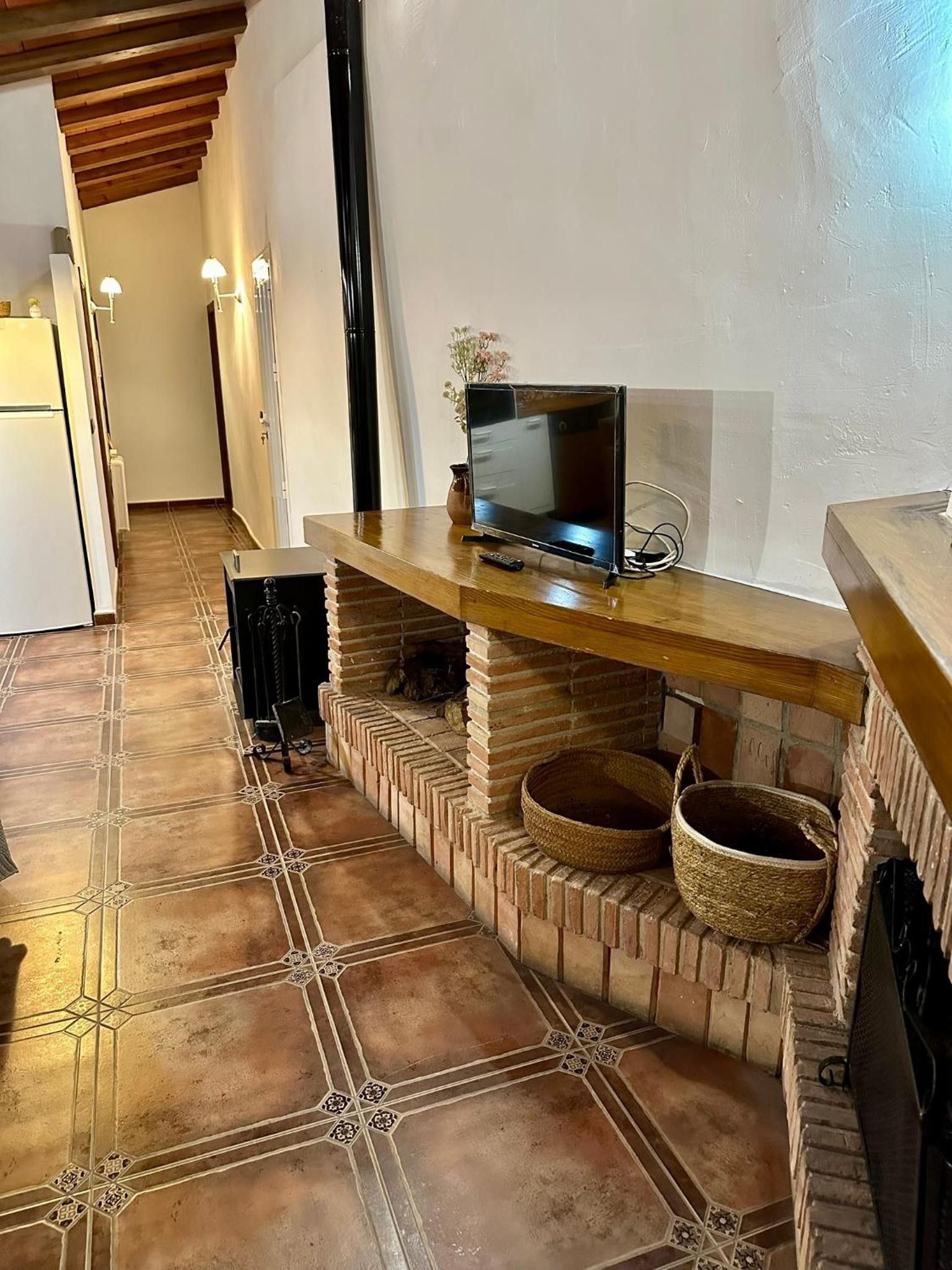 Een keuken met een televisie op een houten plank, een metselwerk schoorsteen en betegelde vloer.